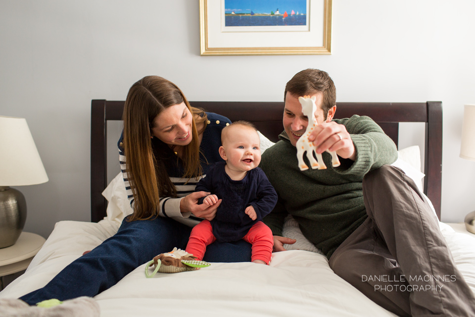 parents on bed with baby and dad holds toy 