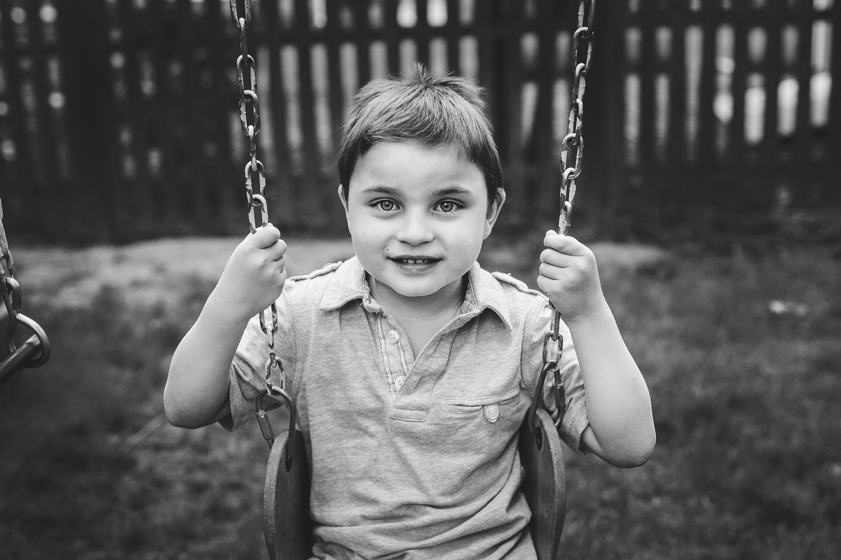 little boy on swing holding on to chains smiling at camera