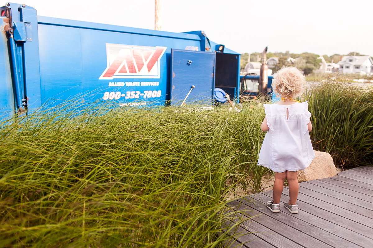 little girl in white dress watching garbage truck