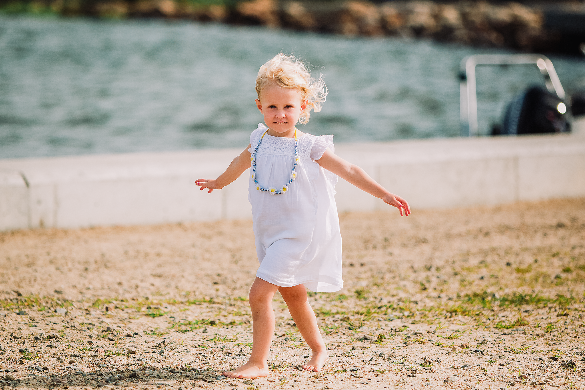 little girl in white dress walking barefoot with arms outstretched