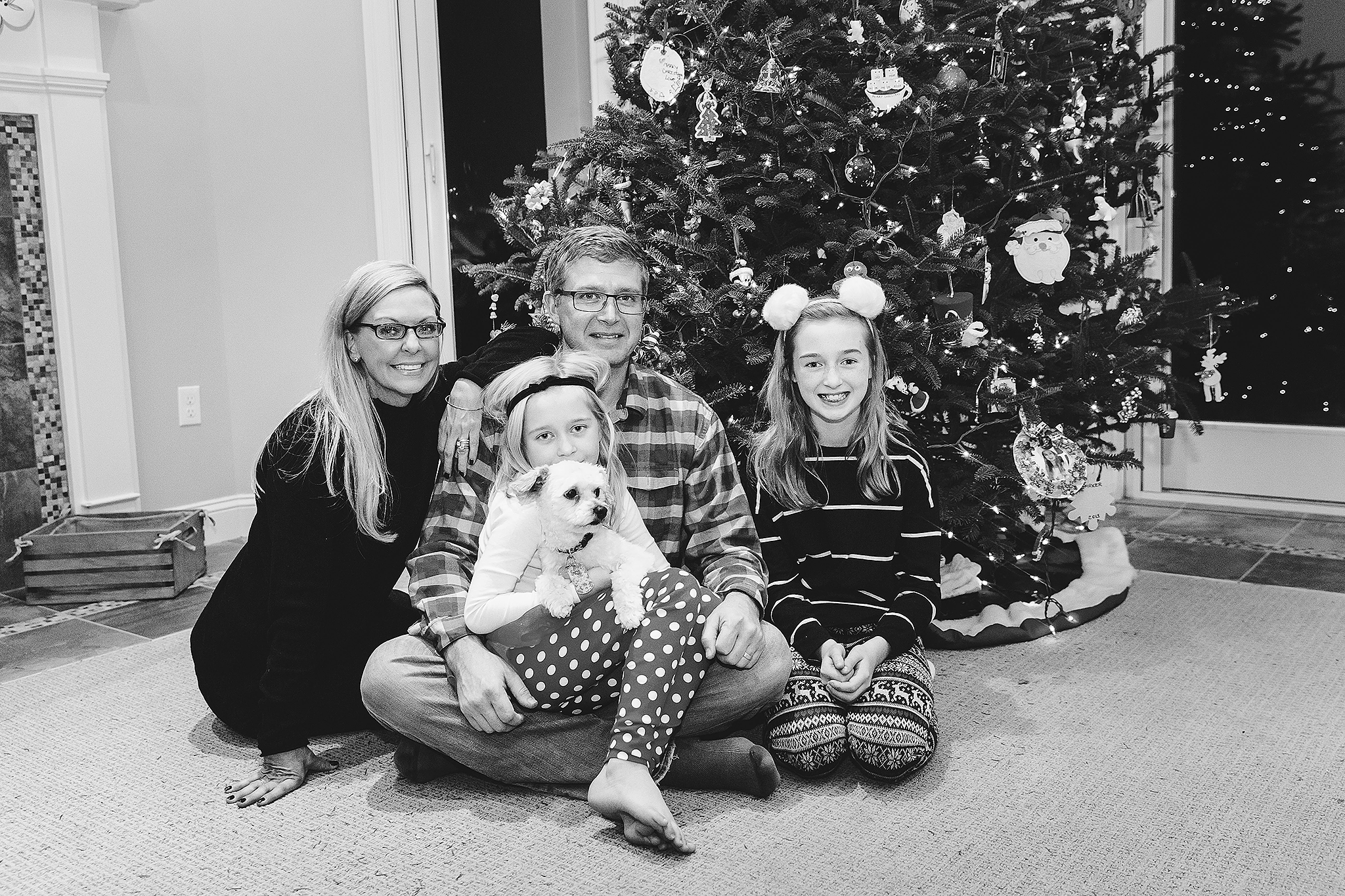 family sitting in front of Christmas Tree with small dog