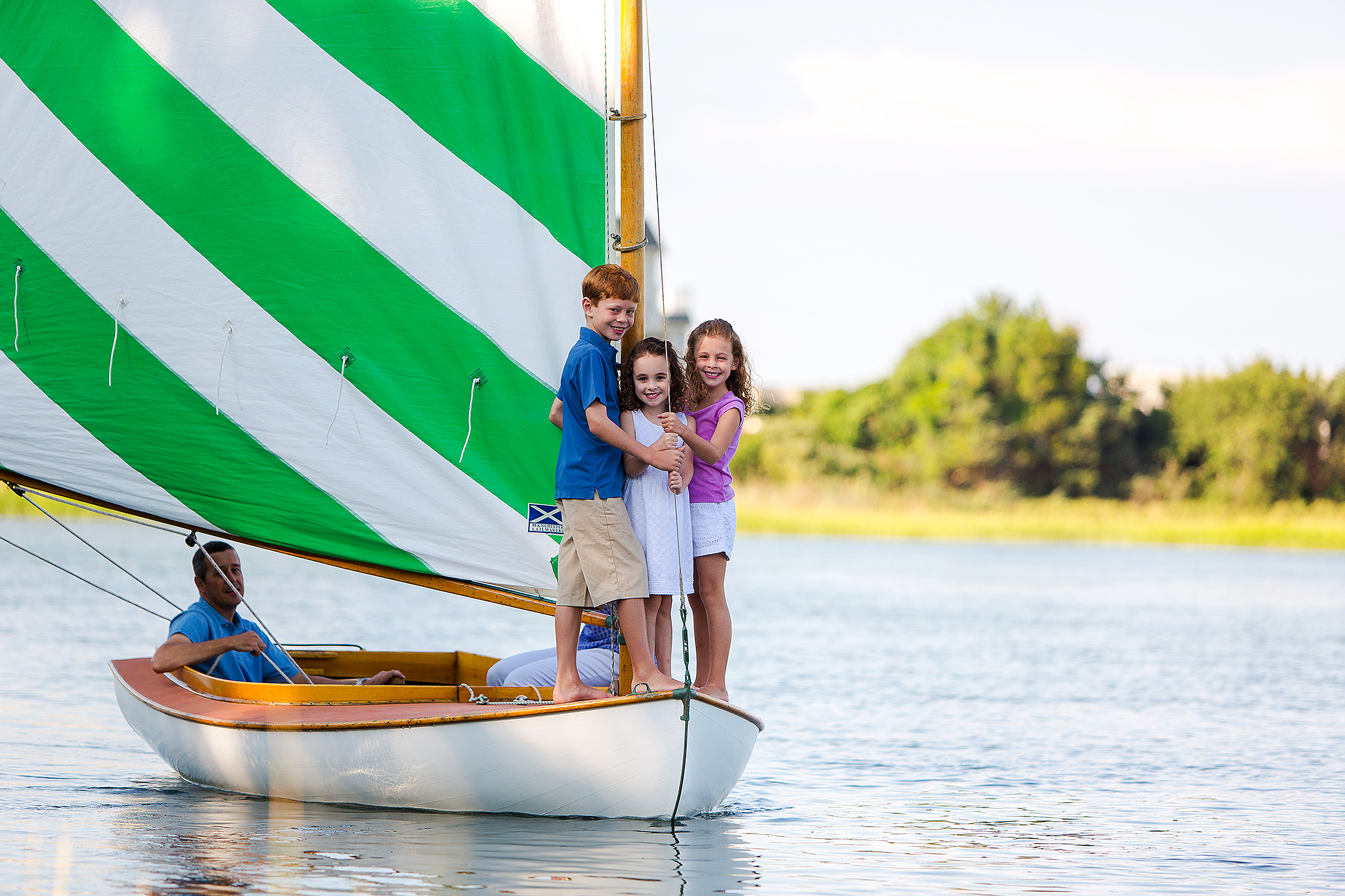 brother and sisters standing in front of sailboat while dad watches