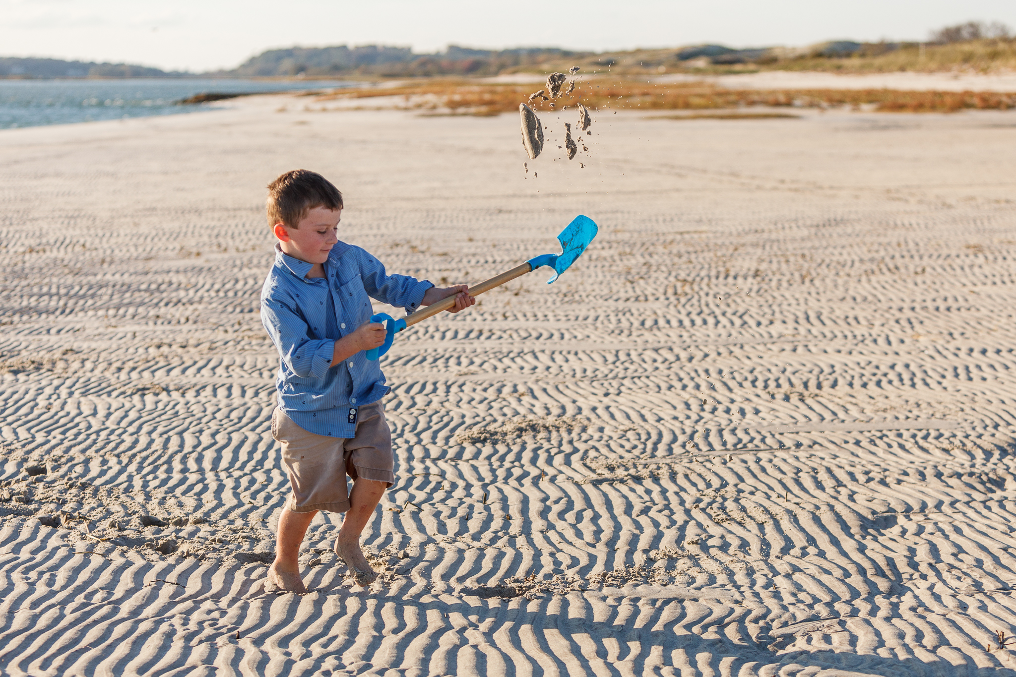 boy on beach flinging sand with a shovel