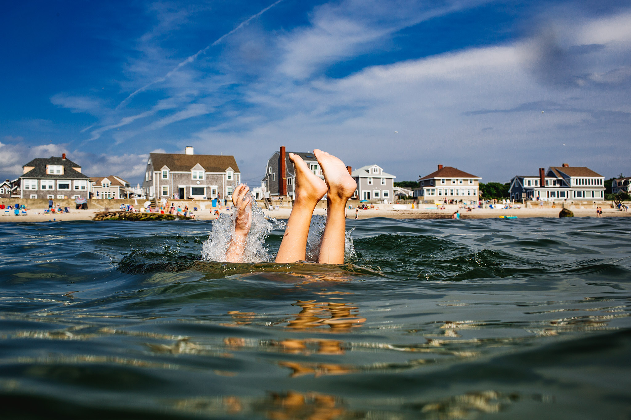 child's feet sticking up above water with beach homes in background