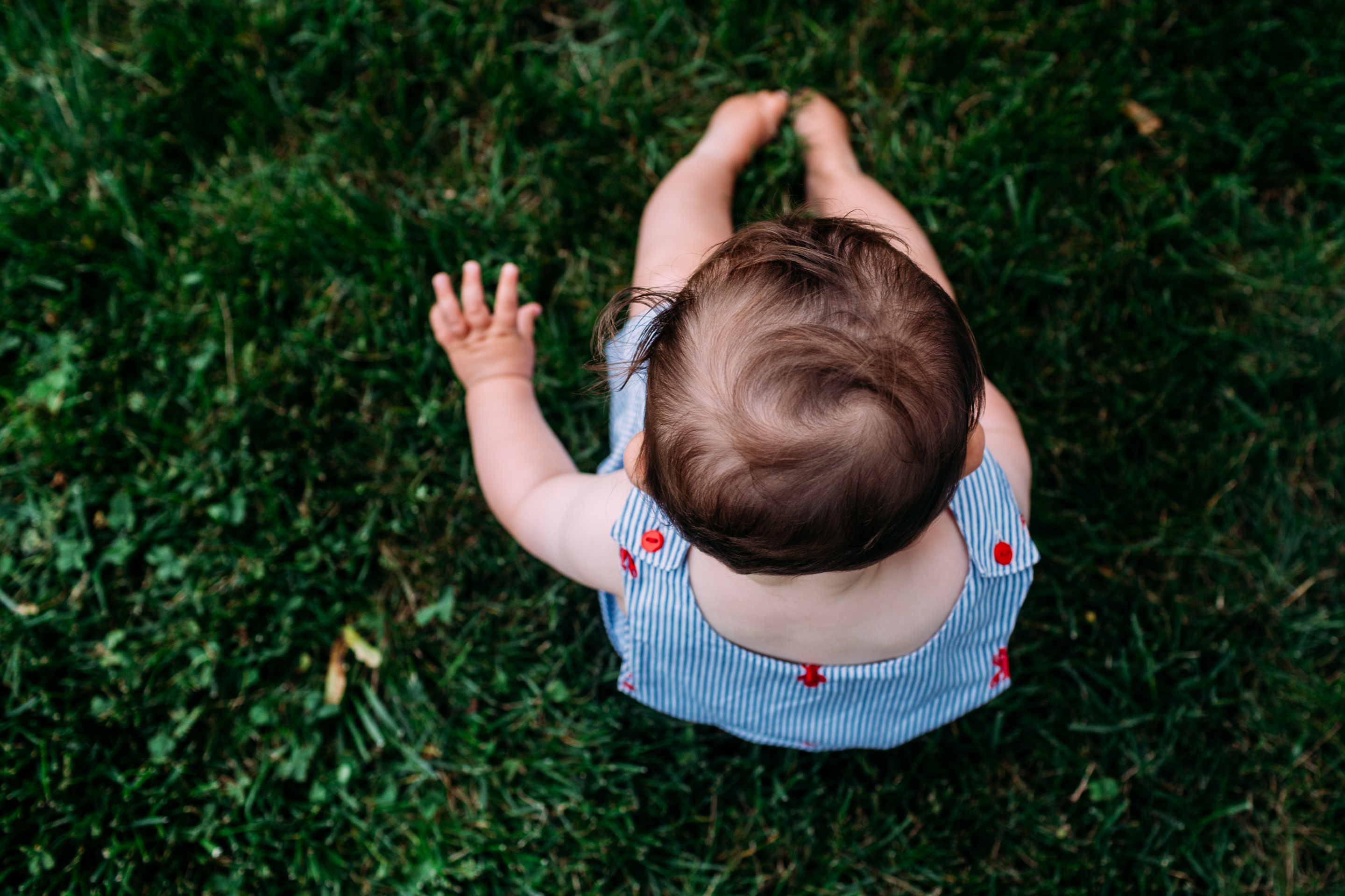 baby boy sitting on grass in overalls