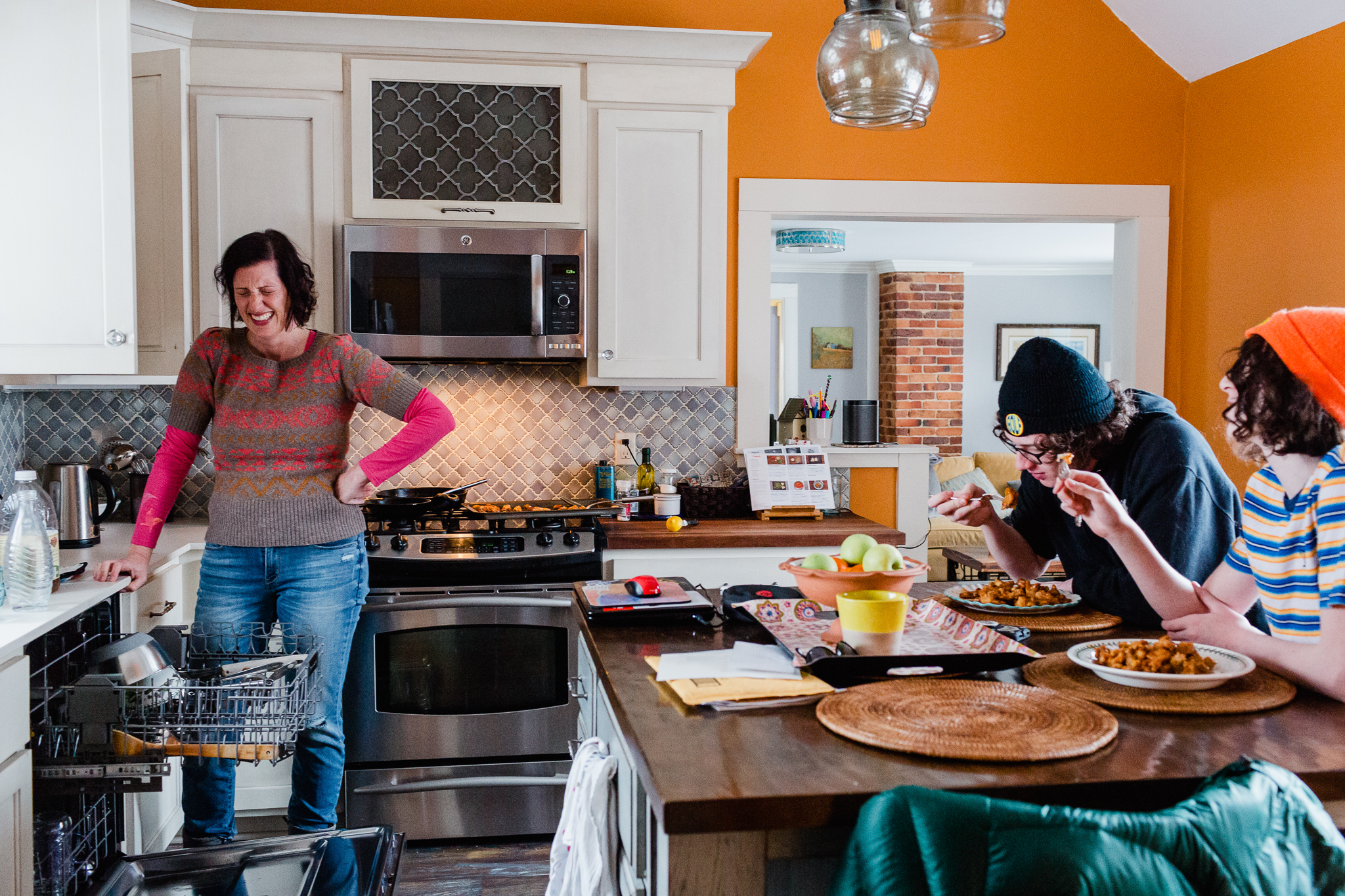 mom laughing in kitchen while two sons eat at counter