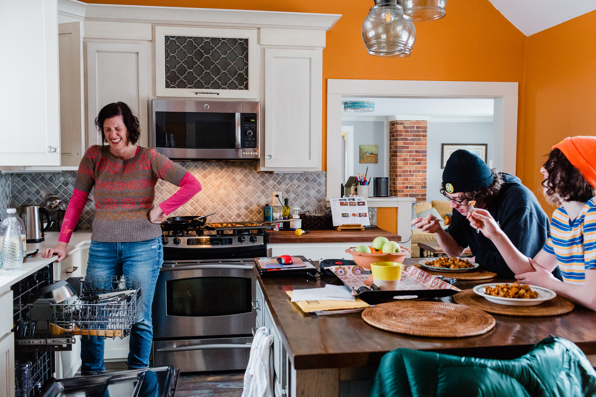 mom standing in kitchen laughing while sons eat at counter