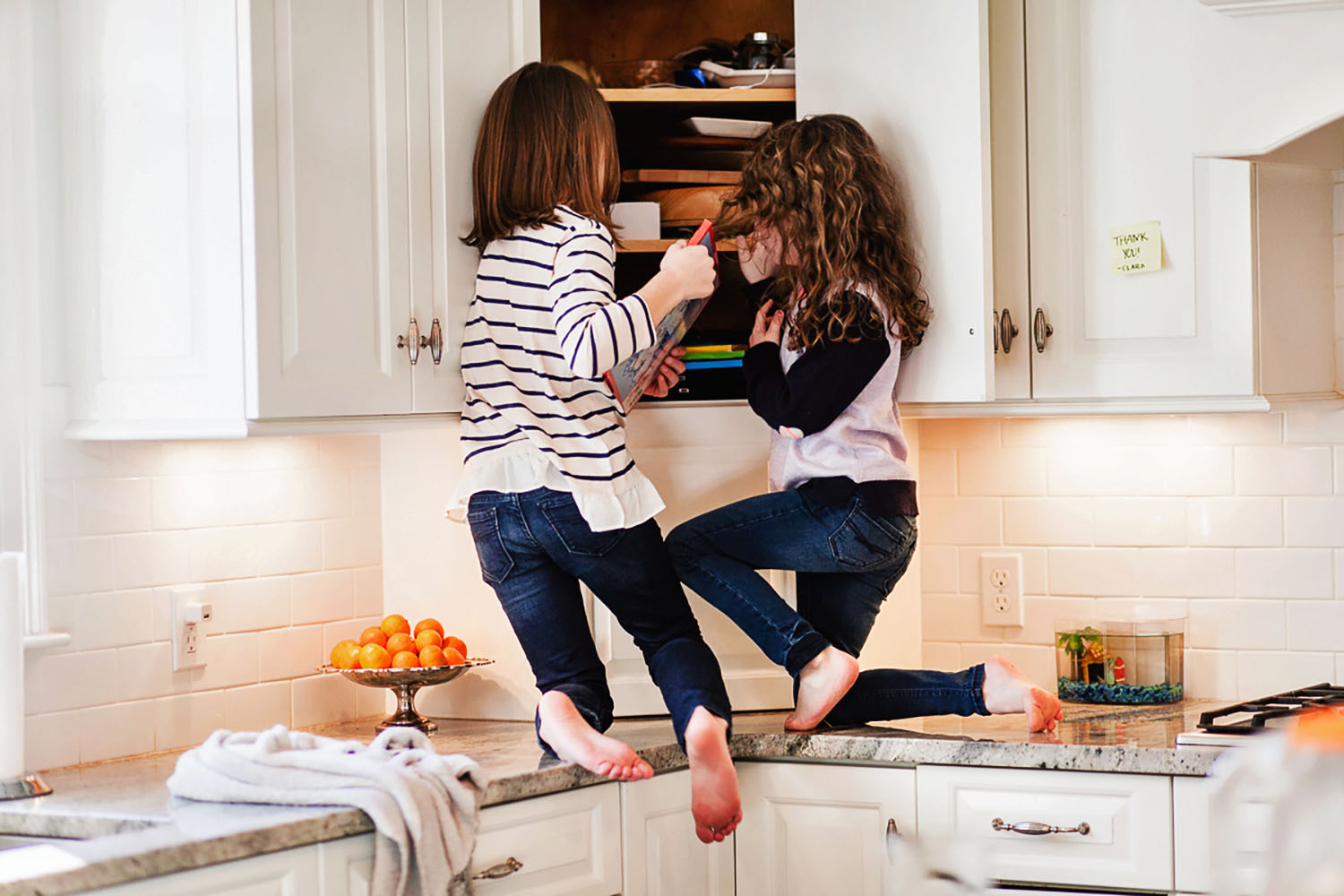 two young girls climbing on the kitchen counter
