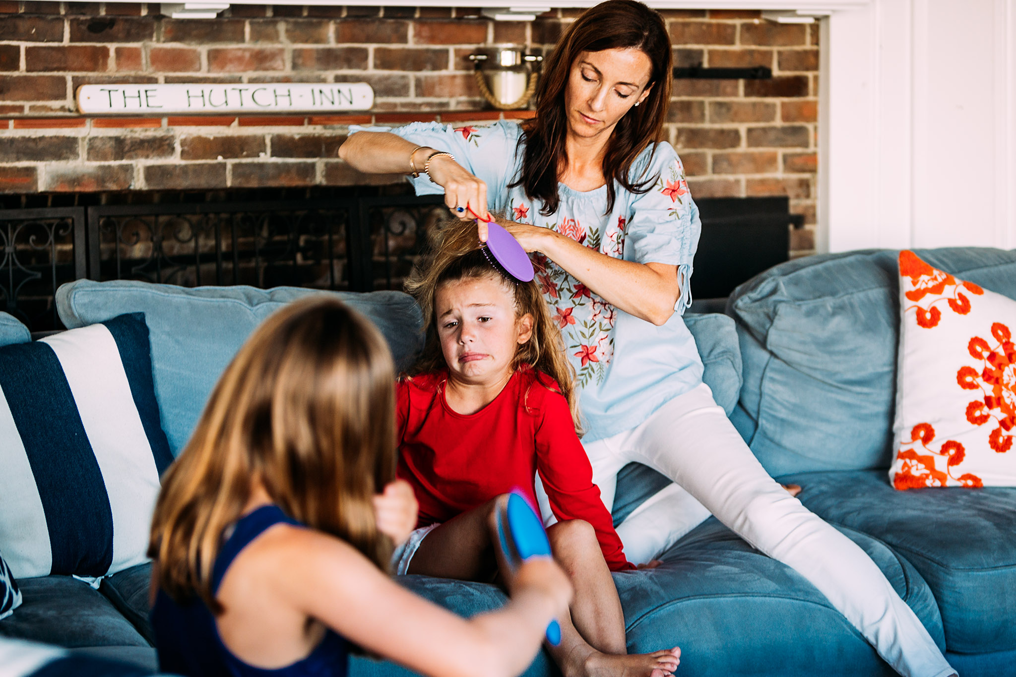 mom brushing hair of little girl making a face