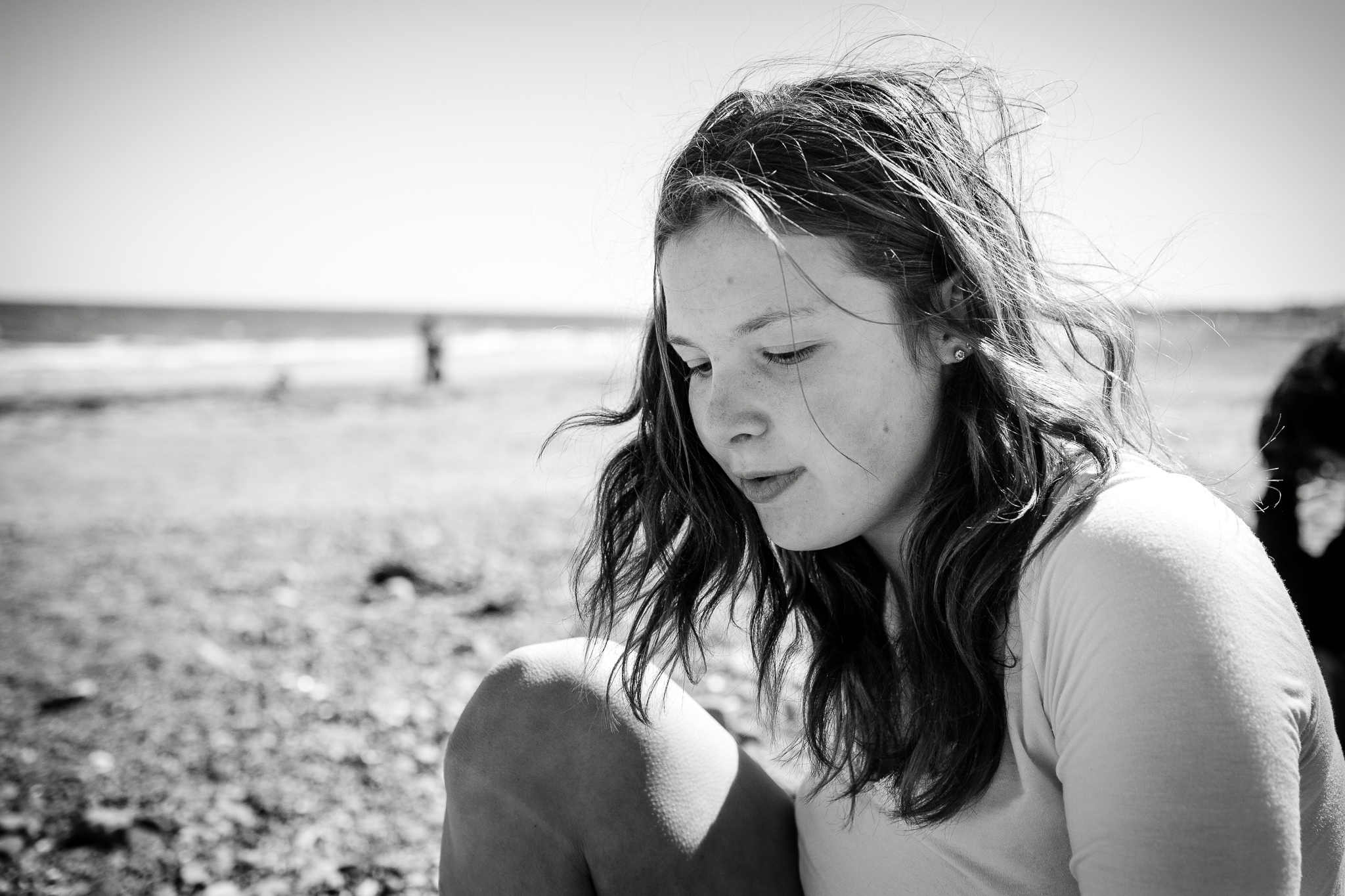teenager sitting on beach with hair blowing