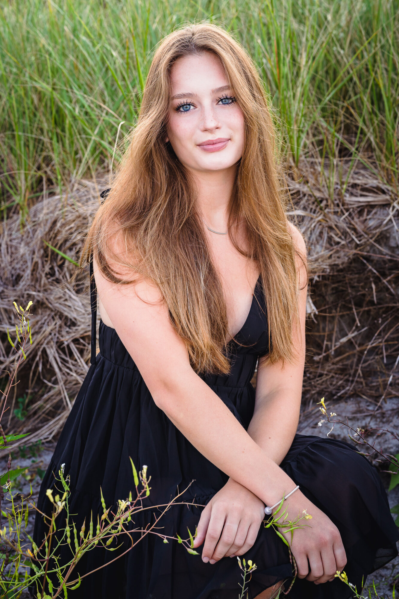 high school senior female with long brown hair kneeling near seagrass