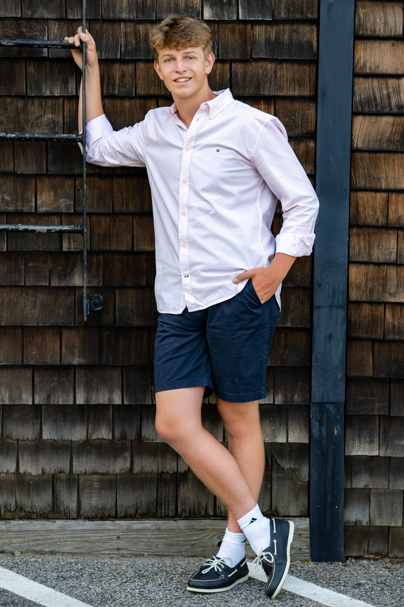 high school senior boy wearing navy shorts and white button down shirt leaning against an iron ladder