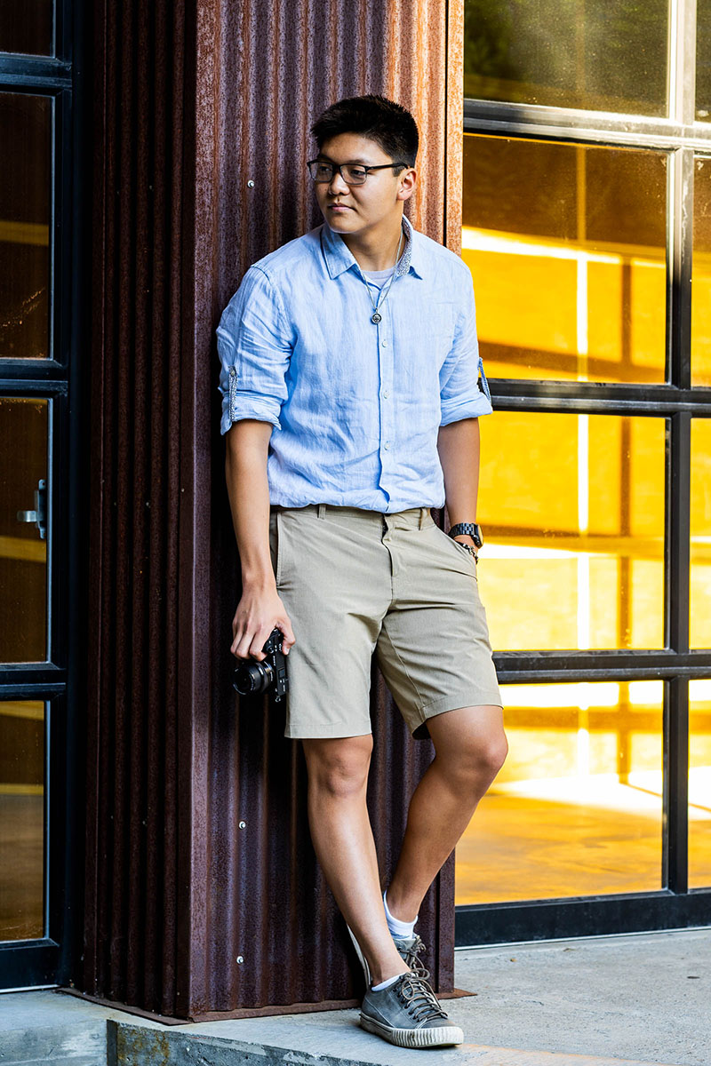 high school senior boy wearing blue shirt and khaki shorts holding a camera