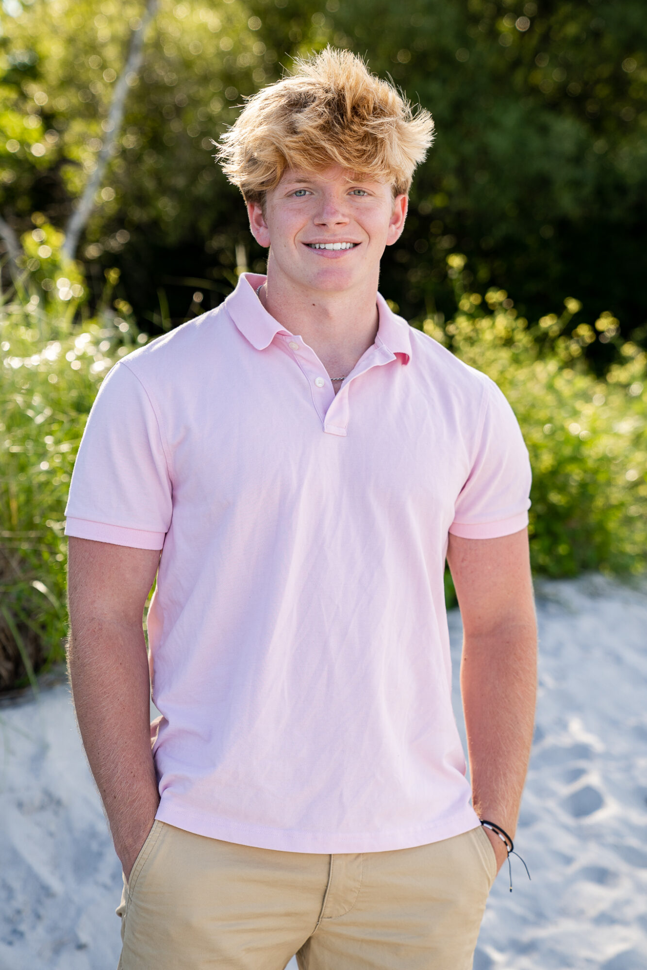 high school senior male wearing pink polo shirt and khaki shorts standing on beach