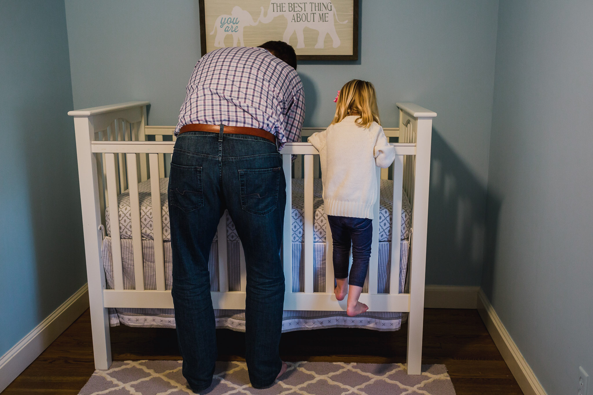 young girl climbing on crib next to father