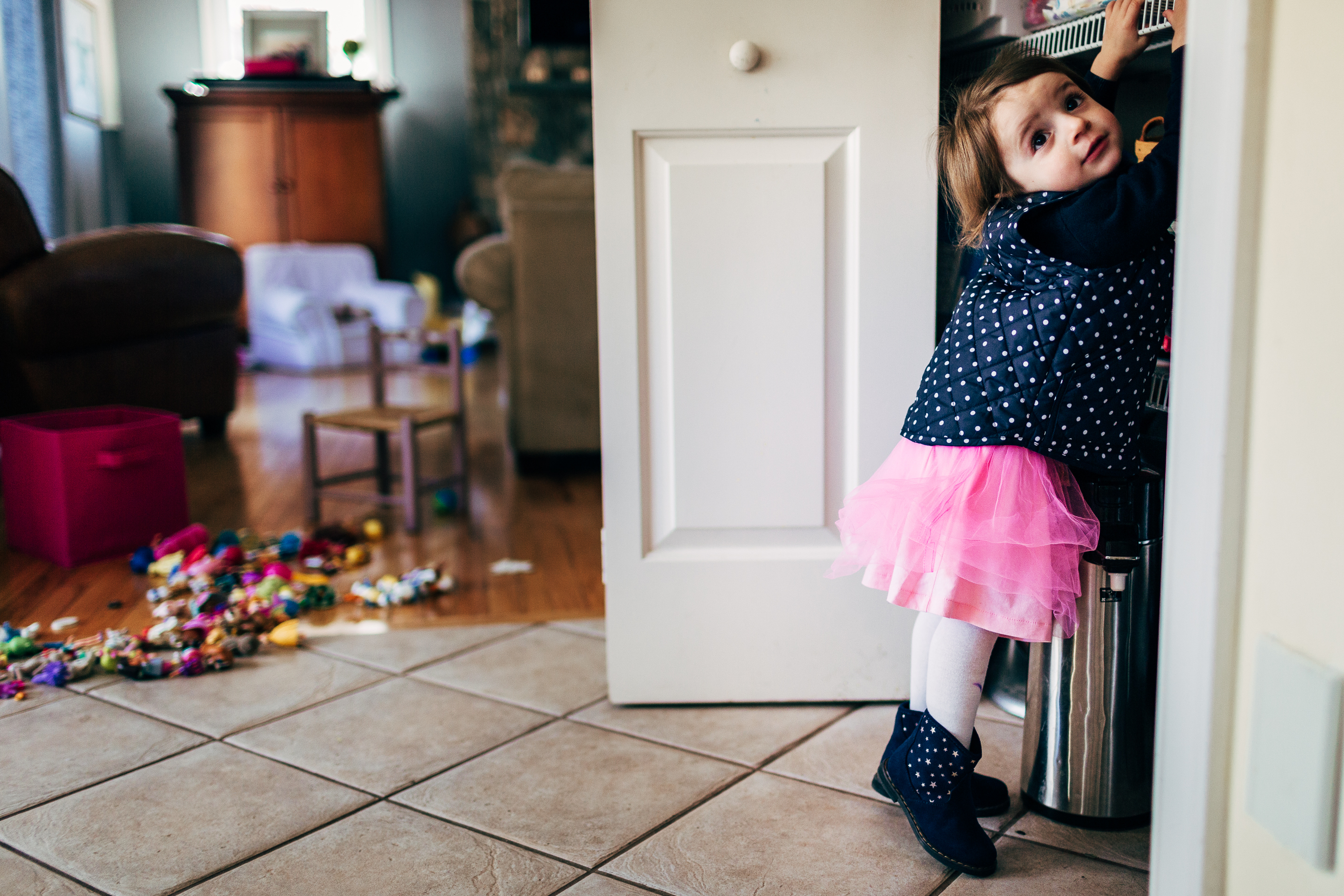little girl in pink tutu and polka dot vest reaching into closet with mess in background