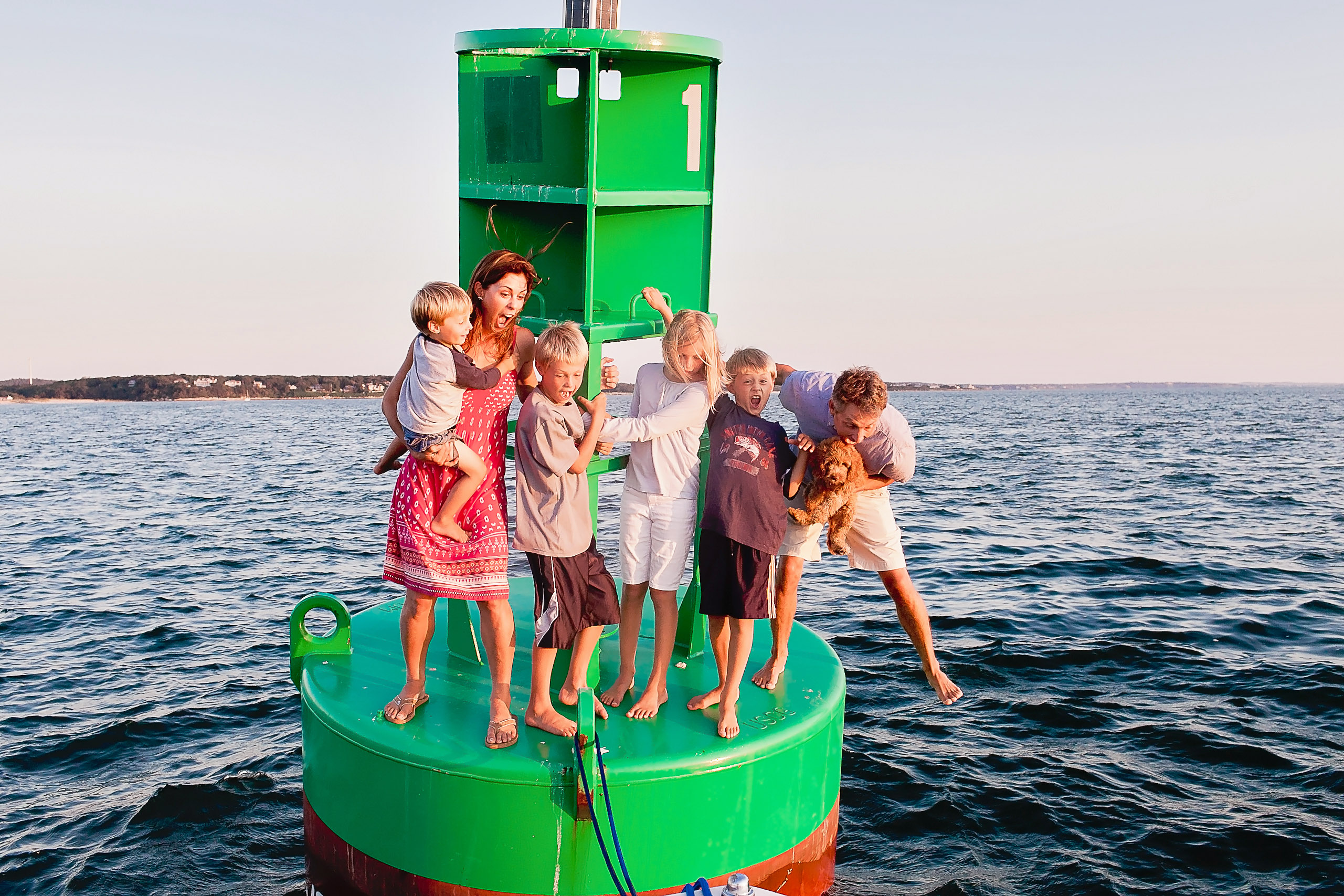 family standing on green buoy in middle of the ocean