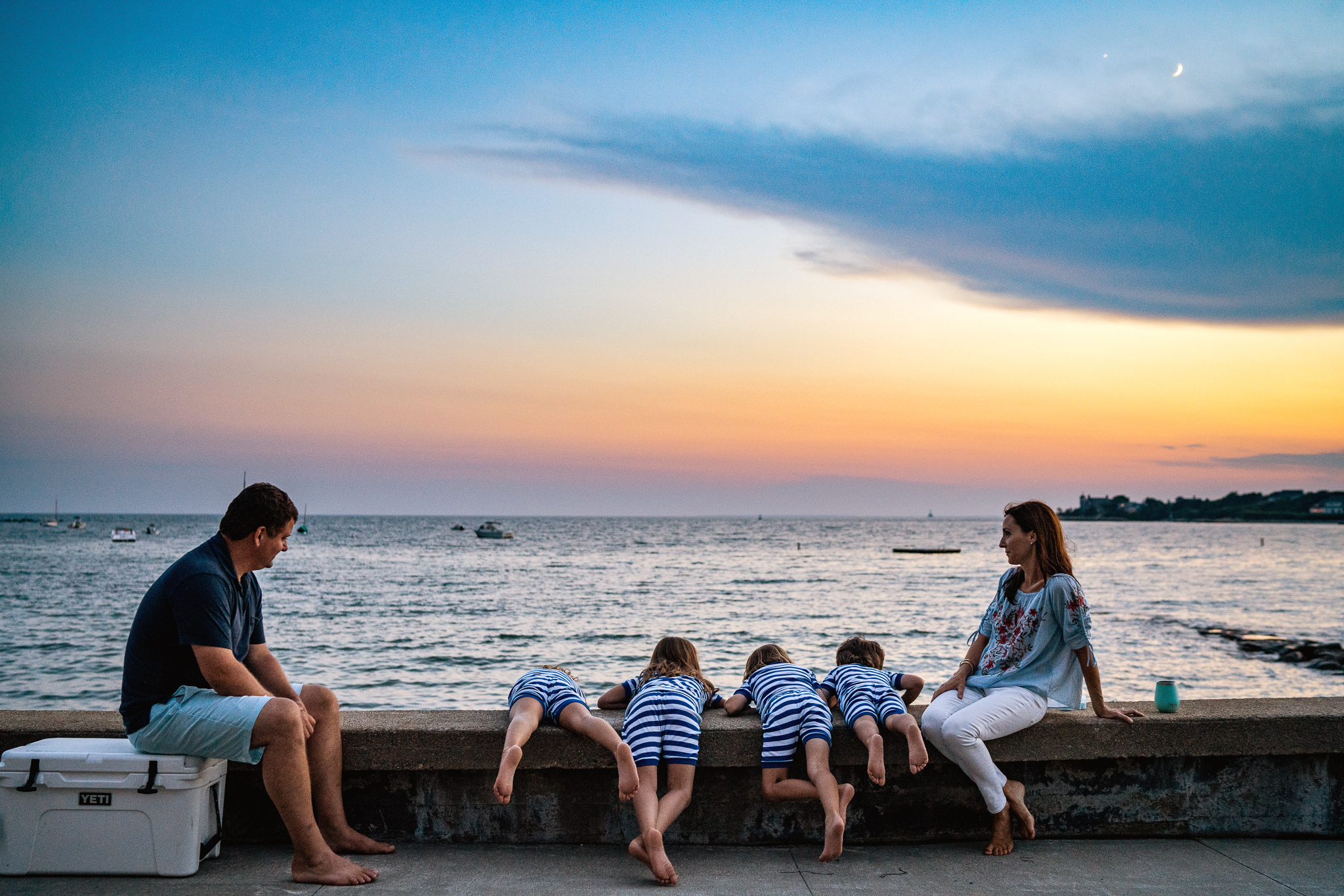 mom and dad sitting on beach wall at sunset with four kids in matching pajamas
