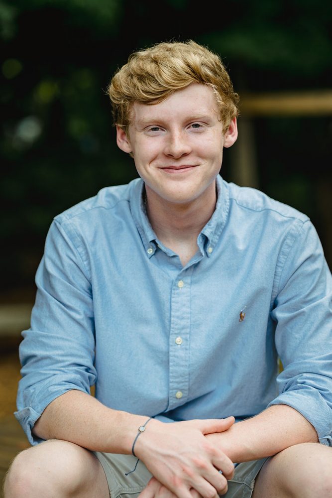 senior boy with blonde hair wearing blue button down shirt smiling
