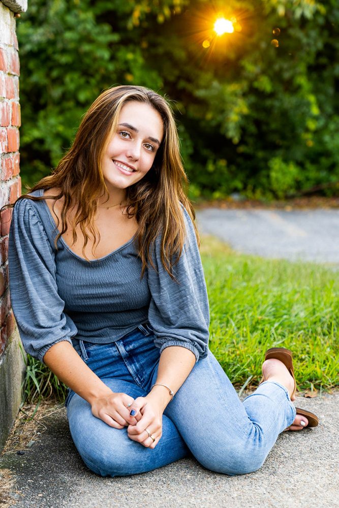 senior girl wearing blue top and jeans smiling at camera