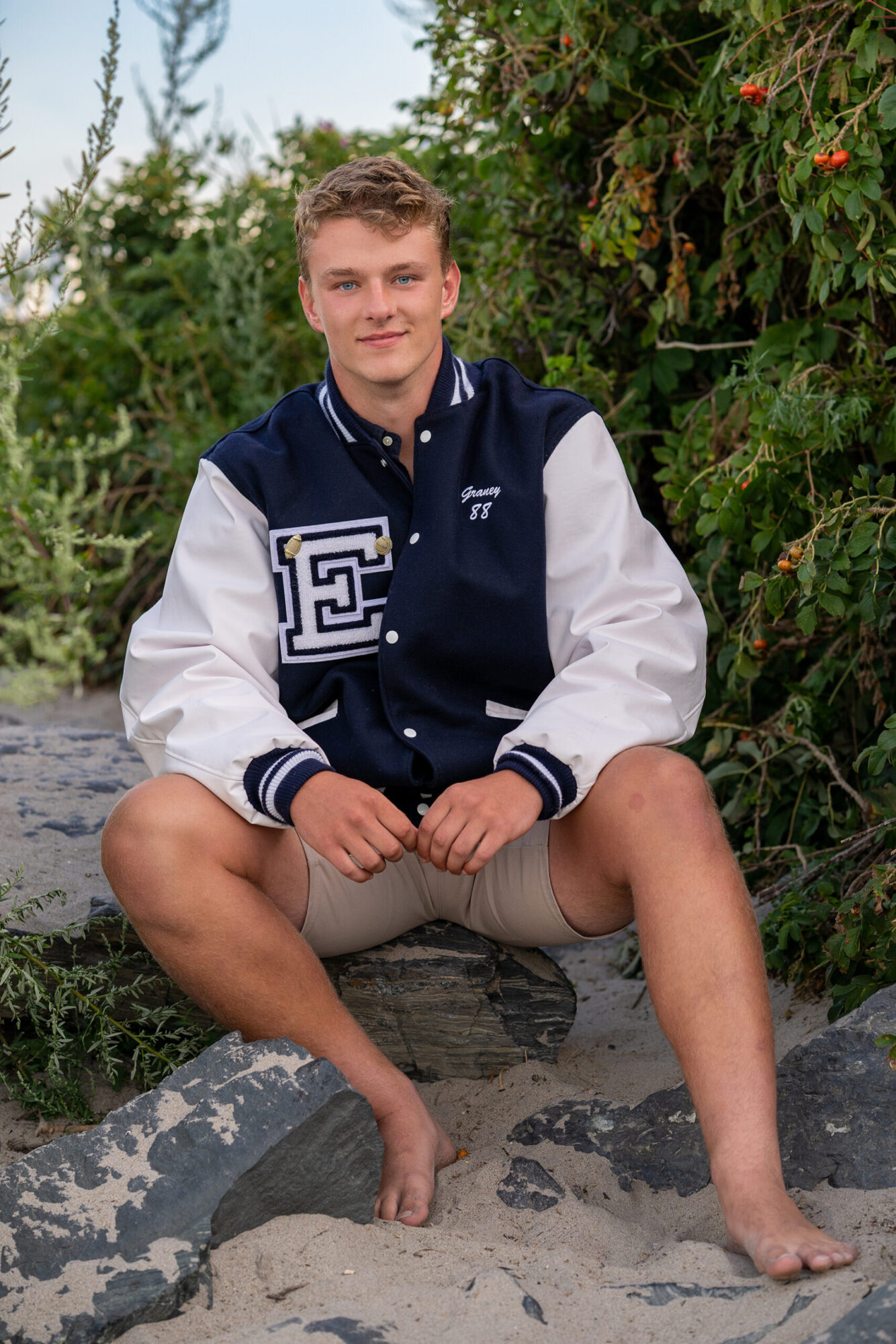 teenage boy wearing a blue and white letterman jacket with an E, smiling