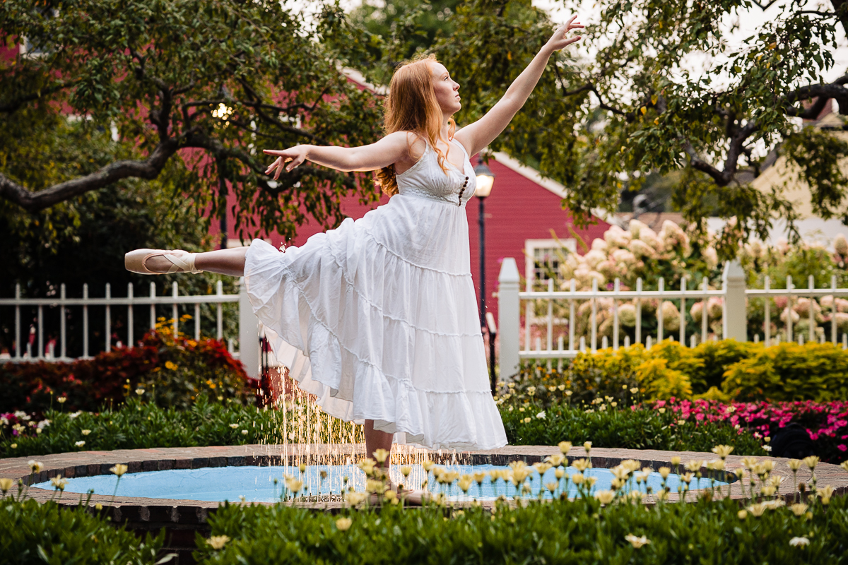 teenage girl wearing ballet slippers and white dress posing near fountain