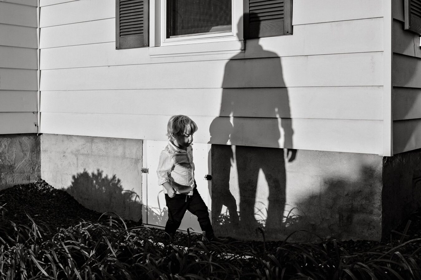 young boy walking past house with shadow of his father